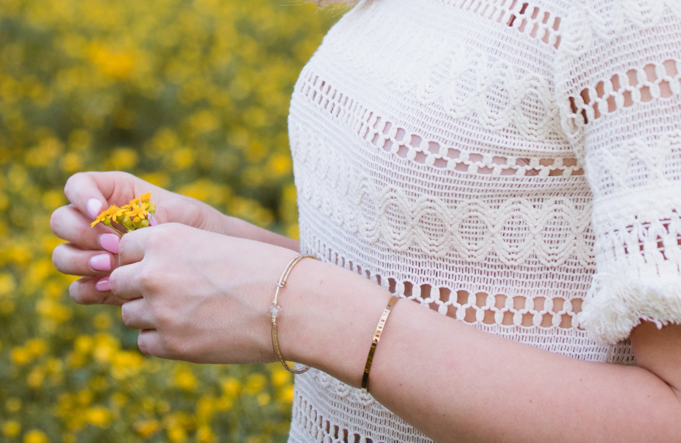 Mulher com blusa branca de renda, segurando pequenas flores amarelas.