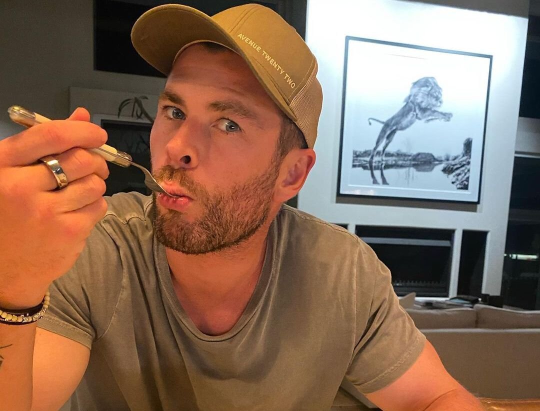 Chris Hemsworth usando boné e com garfo na boca.