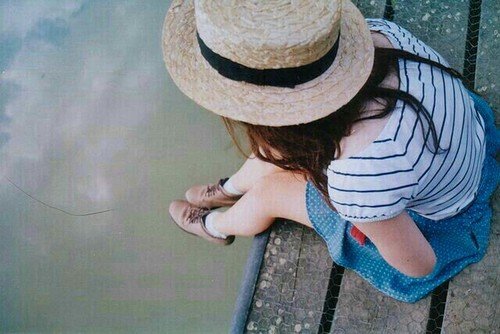 Garota sentada em ponte com pé para baixo olhando para rio abaixo