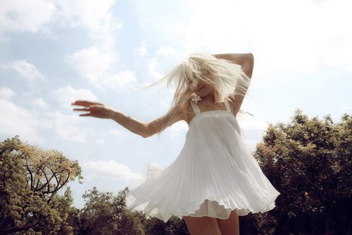 Mulher dançando com vestido branco vista de baixo com céu azul ao fundo