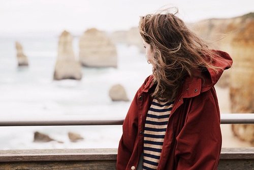 Mulher de costas em ponte olhando paisagem ao fundo com vento nos cabelos