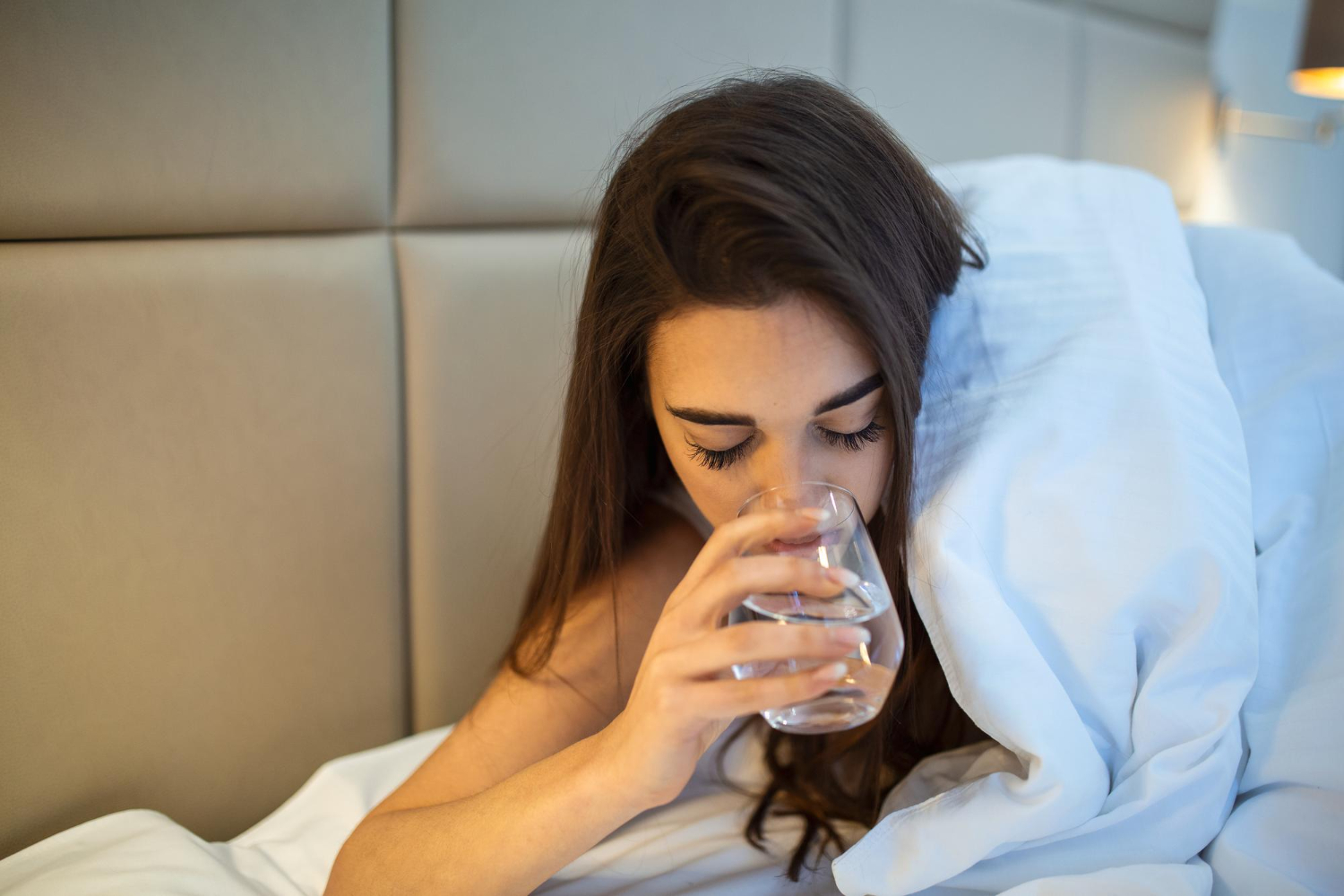 Mulher bebendo um copo de água na cama