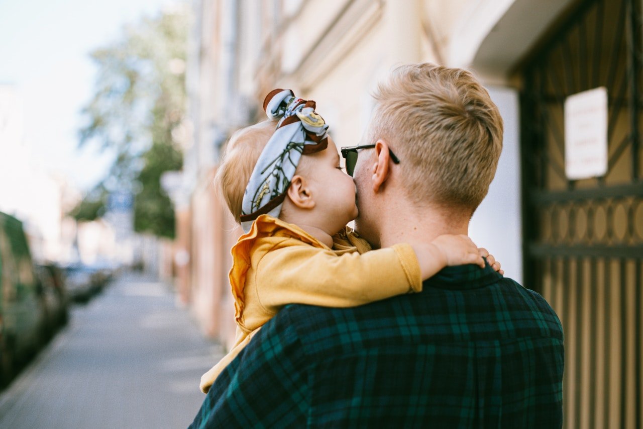 Homem carregando bebê, que está beijando sua bochecha.