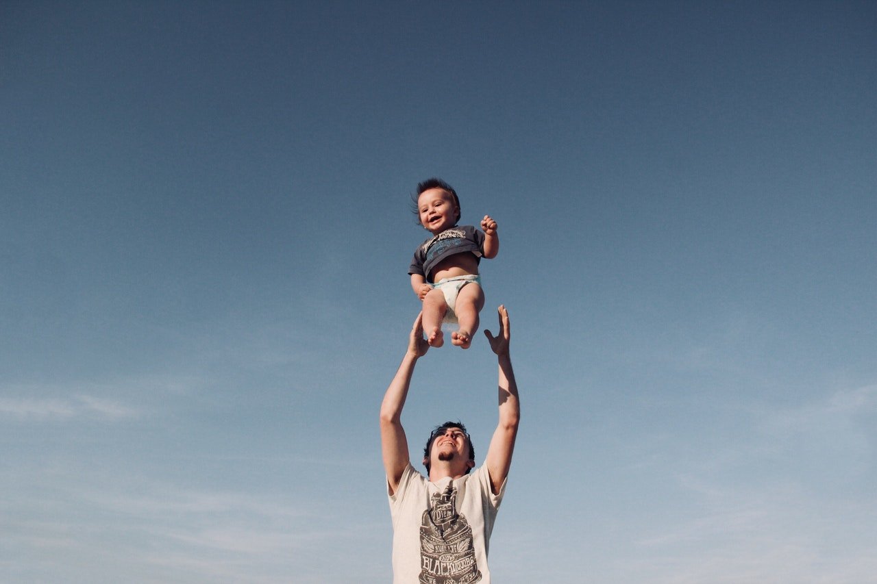 Homem jogando bebê para o alto, que está no ar e rindo.