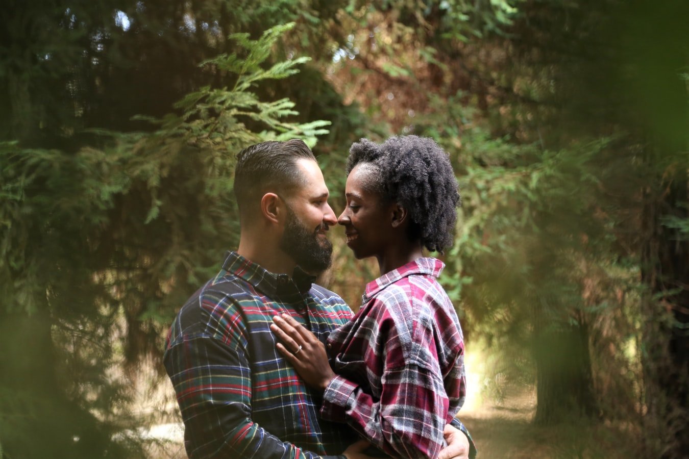 Homem e mulher se abraçando enquanto se olham, no meio de uma floresta.
