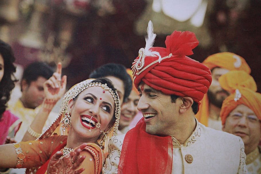 Mulher e homem em casamento indiano. Eles estão lado a lado, e se olham. Ambos usam trajes tradicionais.
