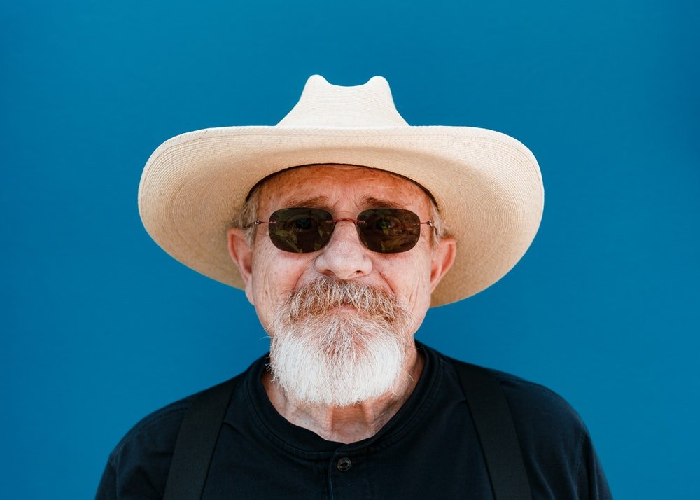 Homem idoso com chapéu de palha e óculos escuros.