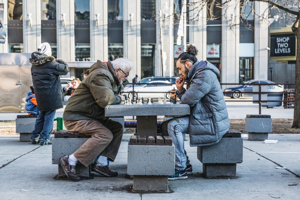 Homem jovem e senhor idoso jogando xadrez na rua.