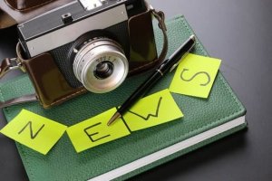 Canva Câmera fotográfica em cima de uma agenda com papeis escritos em inglês 'News'