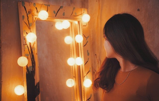Mulher de costas olhando para espelho com luzes em volta