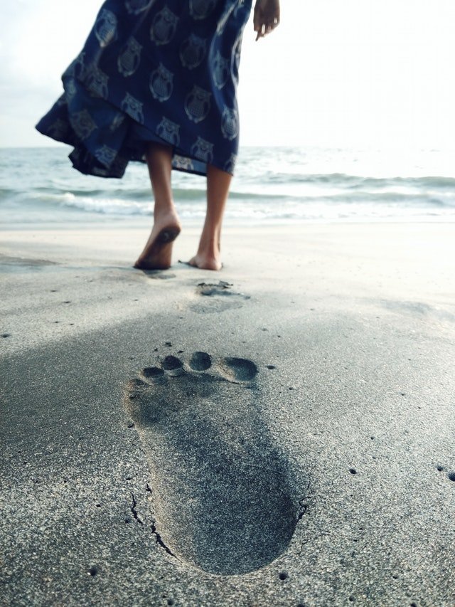 Passos marcados na areia e mulher caminhando para o mar