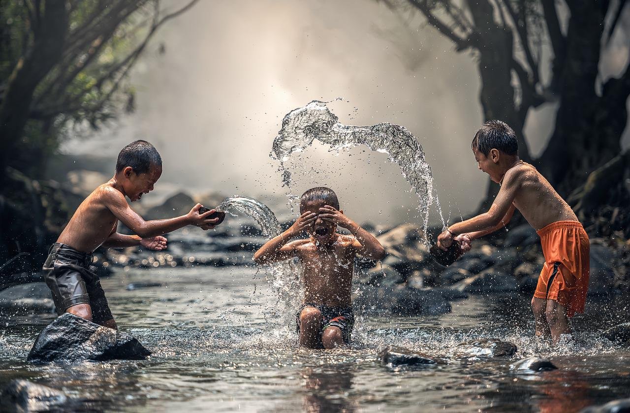 Três crianças brincando e se divertindo com água num rio