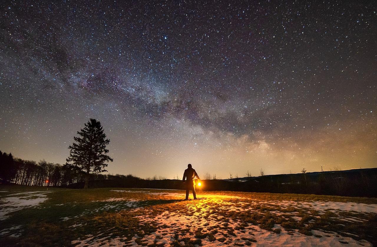 Silhueta de homem diante de céu estrelado em paisagem natural