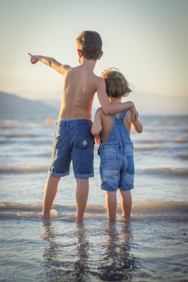 Duas crianças na praia, em pé, enquanto o mais velho aponta para frente