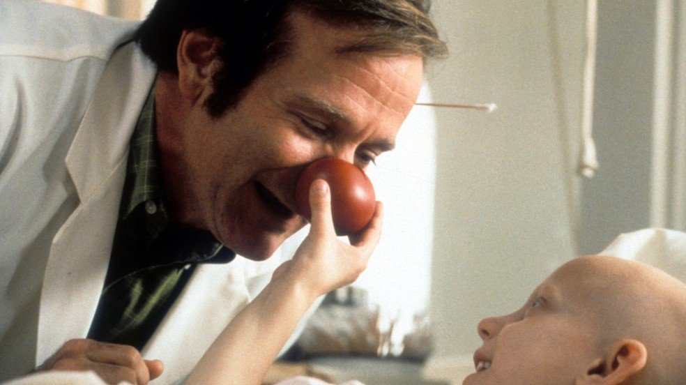 Protagonista do filme tendo seu nariz de palhaço apertado por uma criança doente.