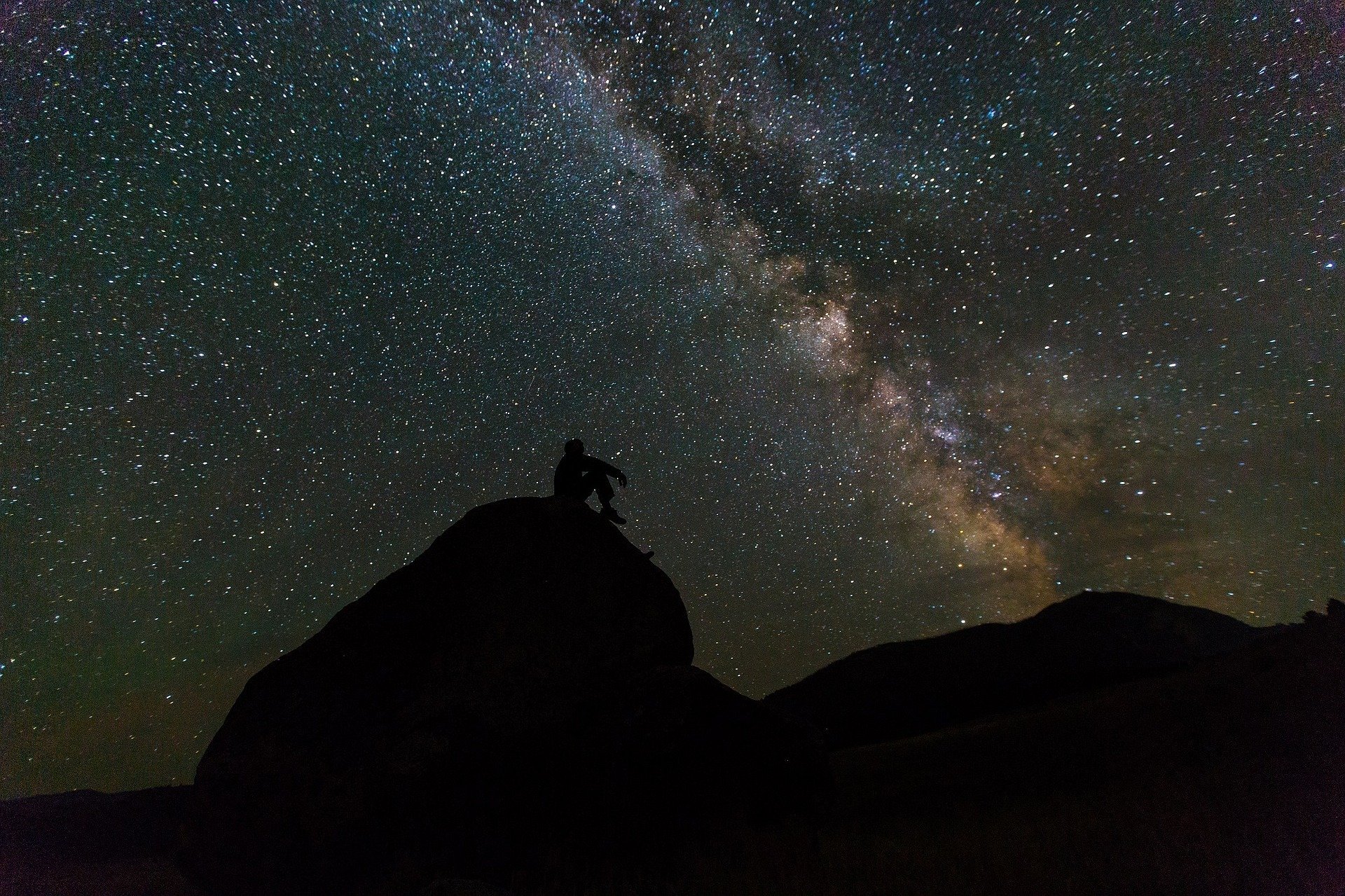Silhueta de homem sentando em uma montanha observando o céu estrelado