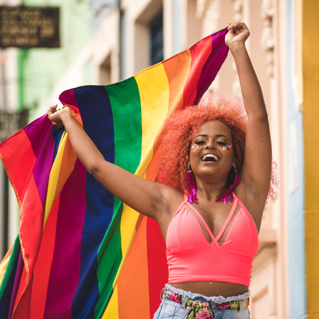 Mulher negra sorrindo e levantando bandeira LGBT.