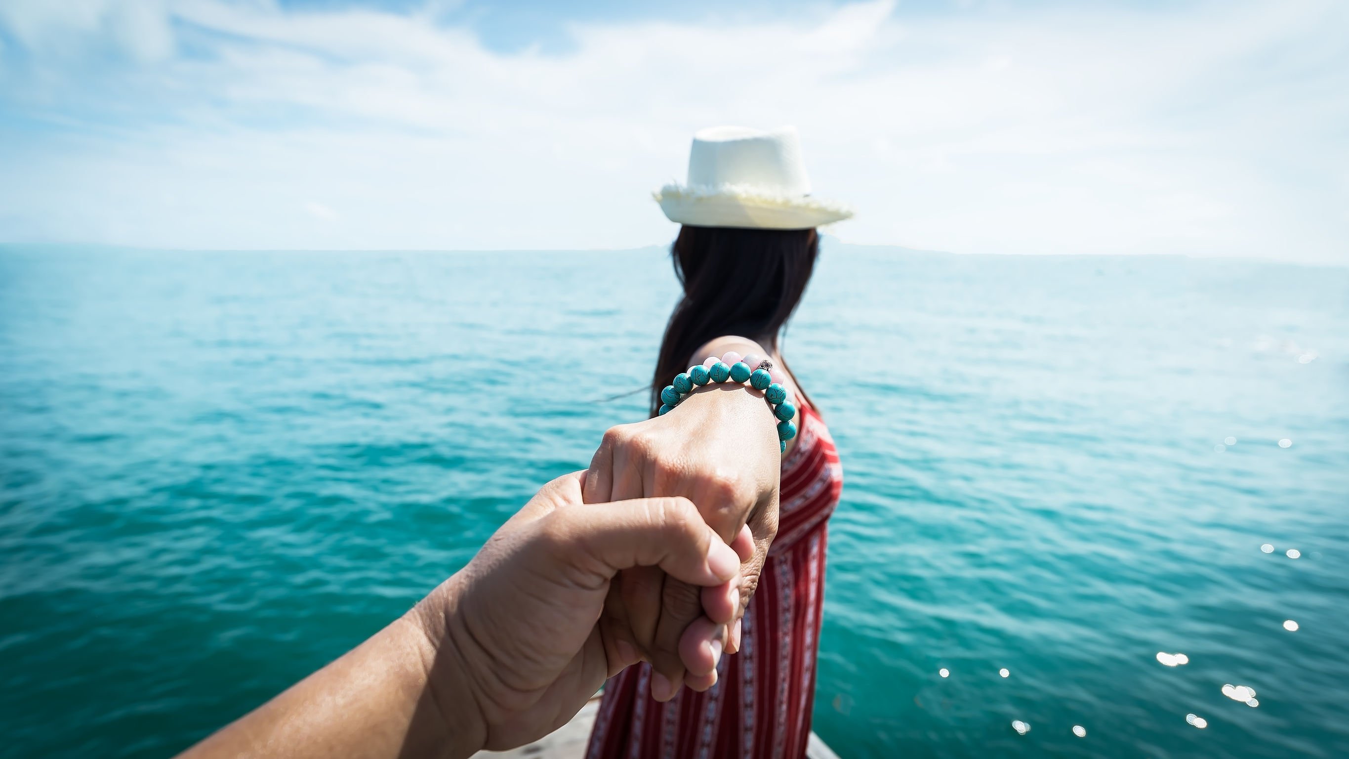 Alguém segurando a mão de uma mulher, que olha para o mar.