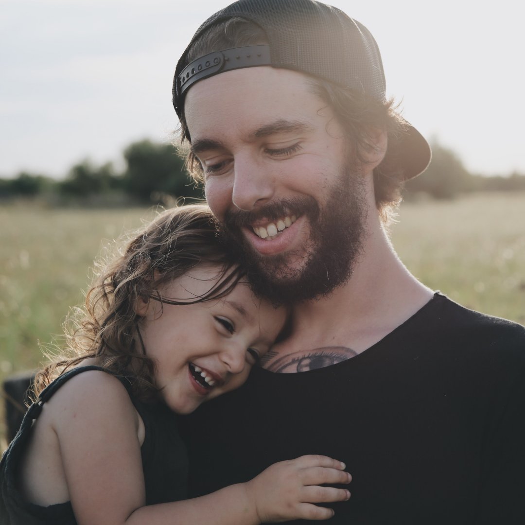 Homem sorrindo abraçando criança no colo