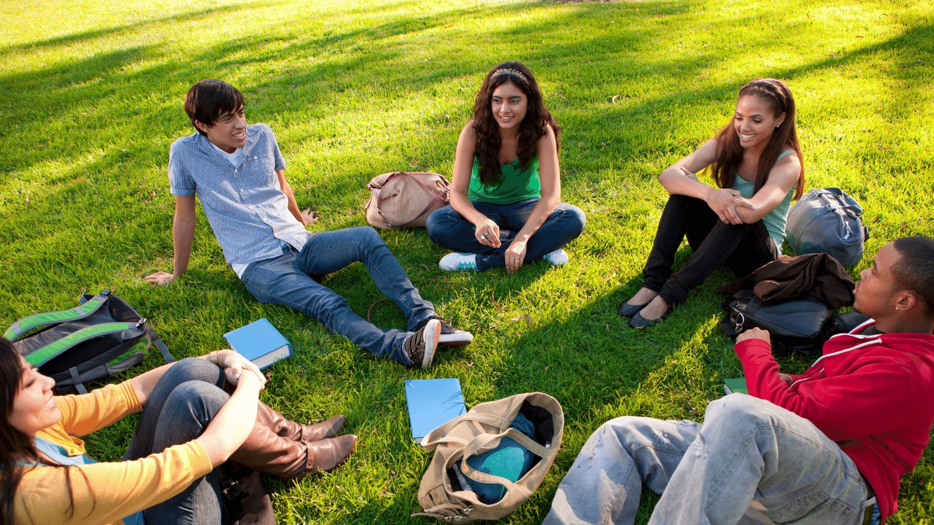 Grupo de amigos sentado em círculo na grama conversando e dando risada