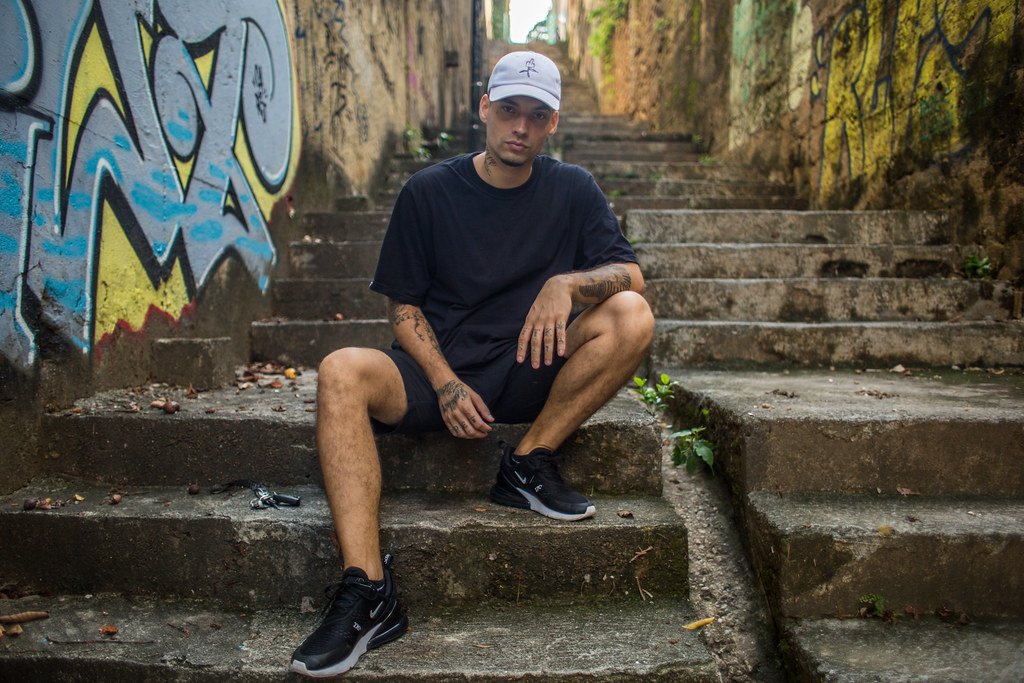 Filipe Ret sentado em escada de rua com grafites e pixos ao fundo