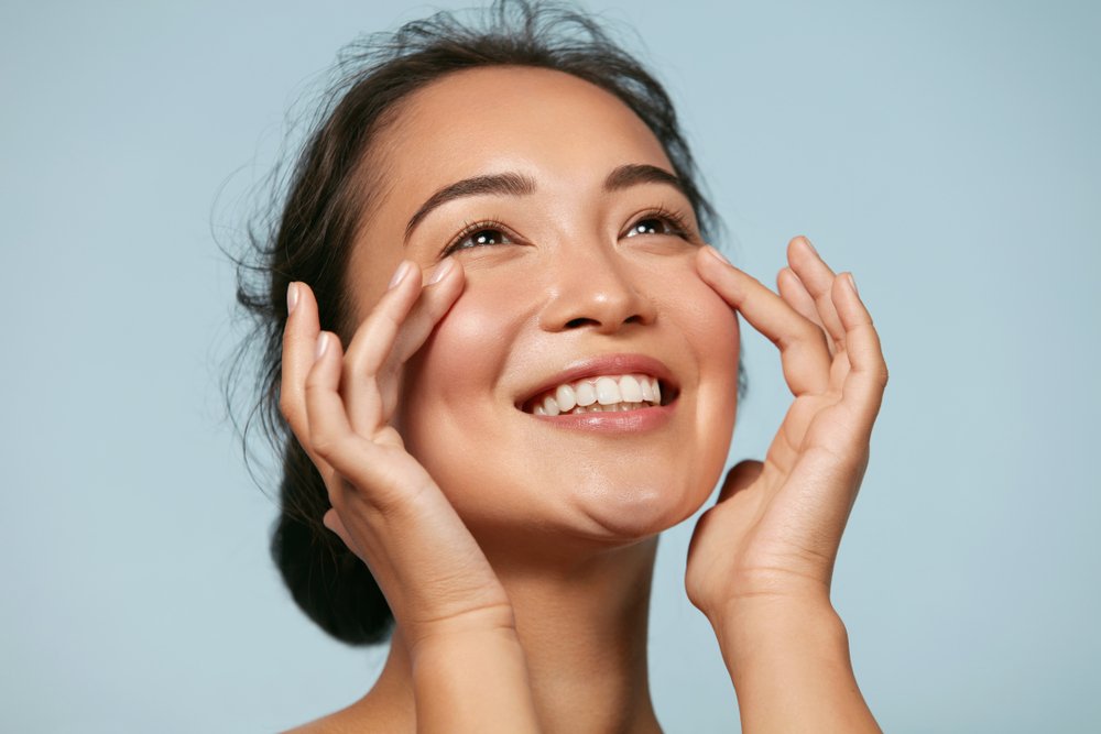 Mulher asiática sorrindo e tocando na pele de seu próprio rosto