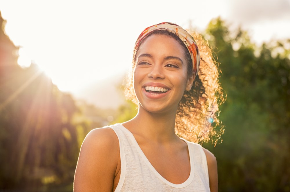 mulher afro-americana sorrindo e olhando para o parque durante o pôr do sol.