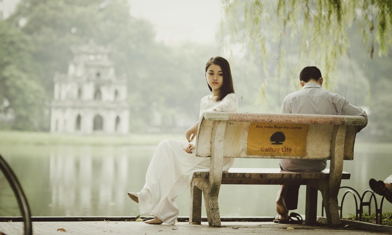 Homem e mulher sentados em banco em uma praça.