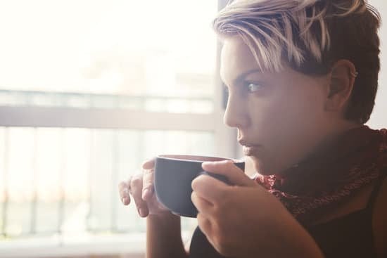 Mulher segurando xícara de café e olhando para a janela ao seu lado