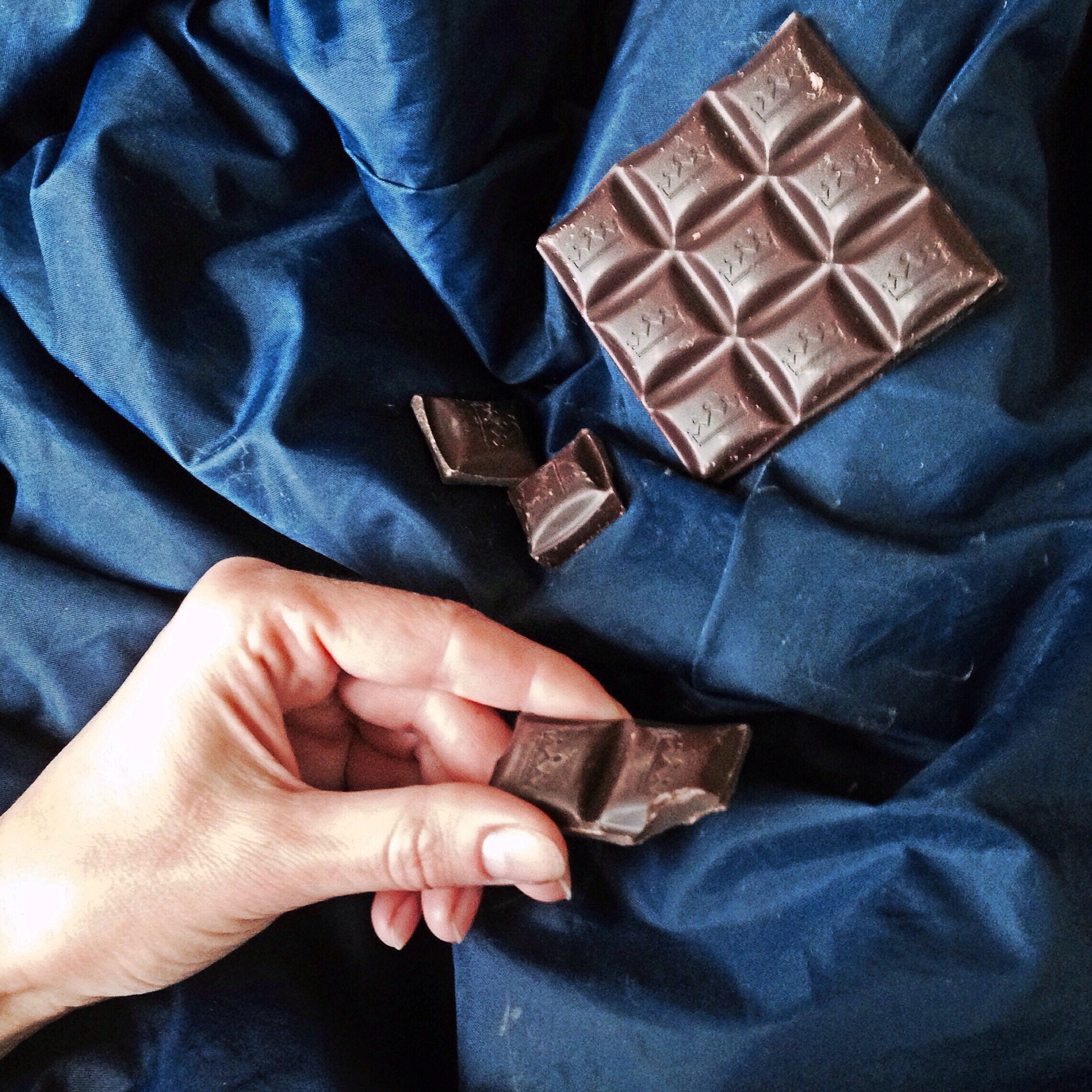 Pessoa segurando pedaço de chocolate e ao lado de uma barra de chocolate