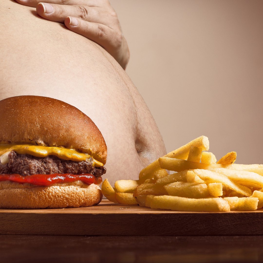 Foto de um hamburguer e fritas com uma pessoa acima do peso atrás