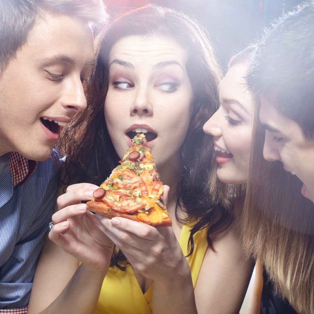 Mulher comendo pizza e outras pessoas cobiçando ao lado