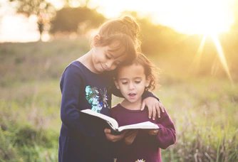 Crianças abraçadas com bíblia nas mãos no campo