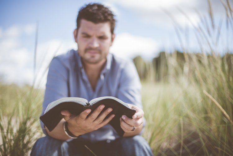 Homem sentado lendo bíblia no campo