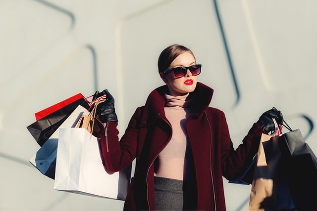 Mulher com óculos escuro e sacolas de compras na mão
