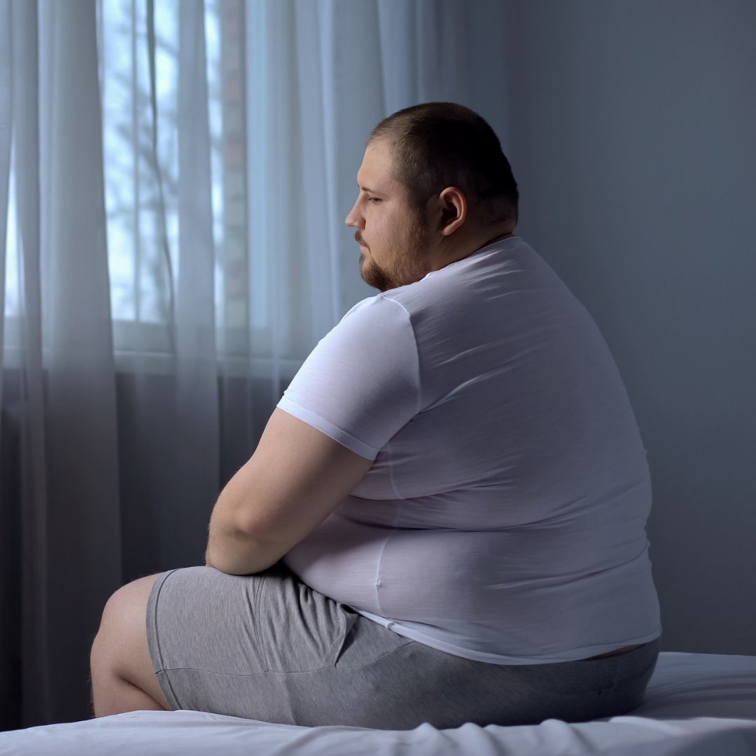 Homem obeso sentado na beira da cama