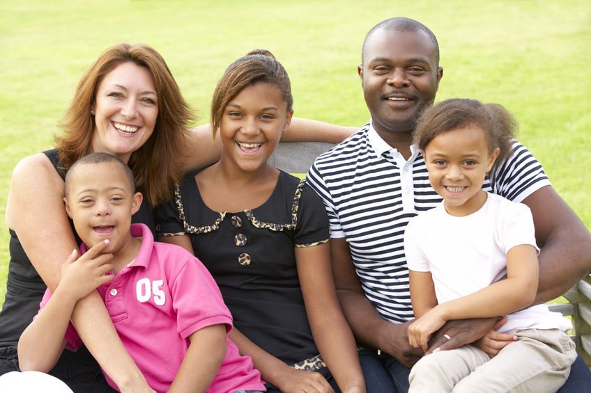 Família sentada em banco com grama ao fundo sorrindo com um dos filhos com Síndrome de Down