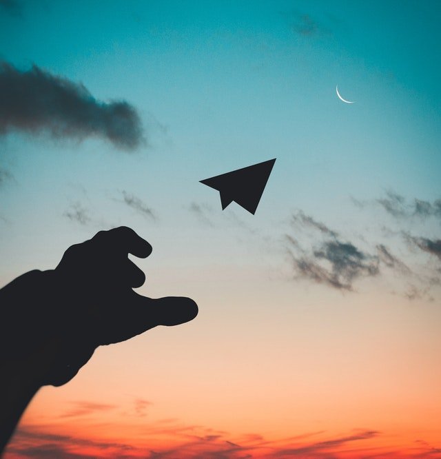 Silhueta de mão com avião de papel voando e céu ao sunset ao fundo