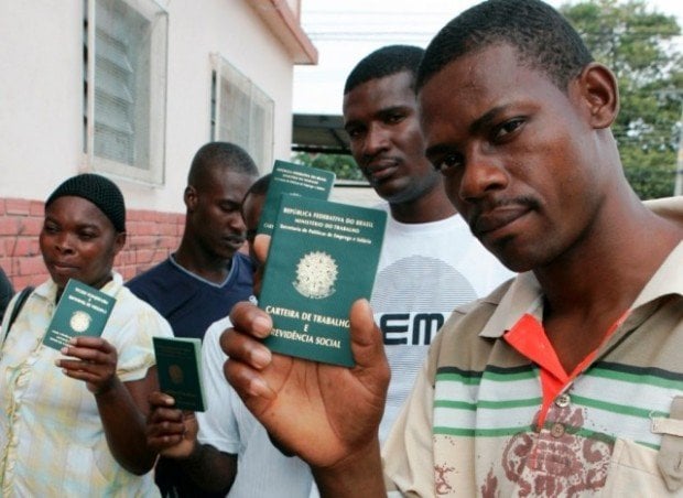 Haitianos segurando suas Carteiras de Trabalho do Brasil.