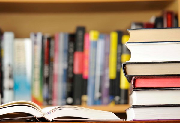 Livro aberto em mesa e livros empilhados