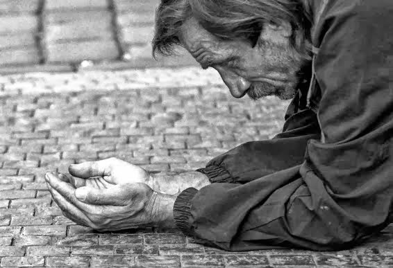Morado de rua ajoelhado no chão, com as mãos estendidas, pedindo ajuda
