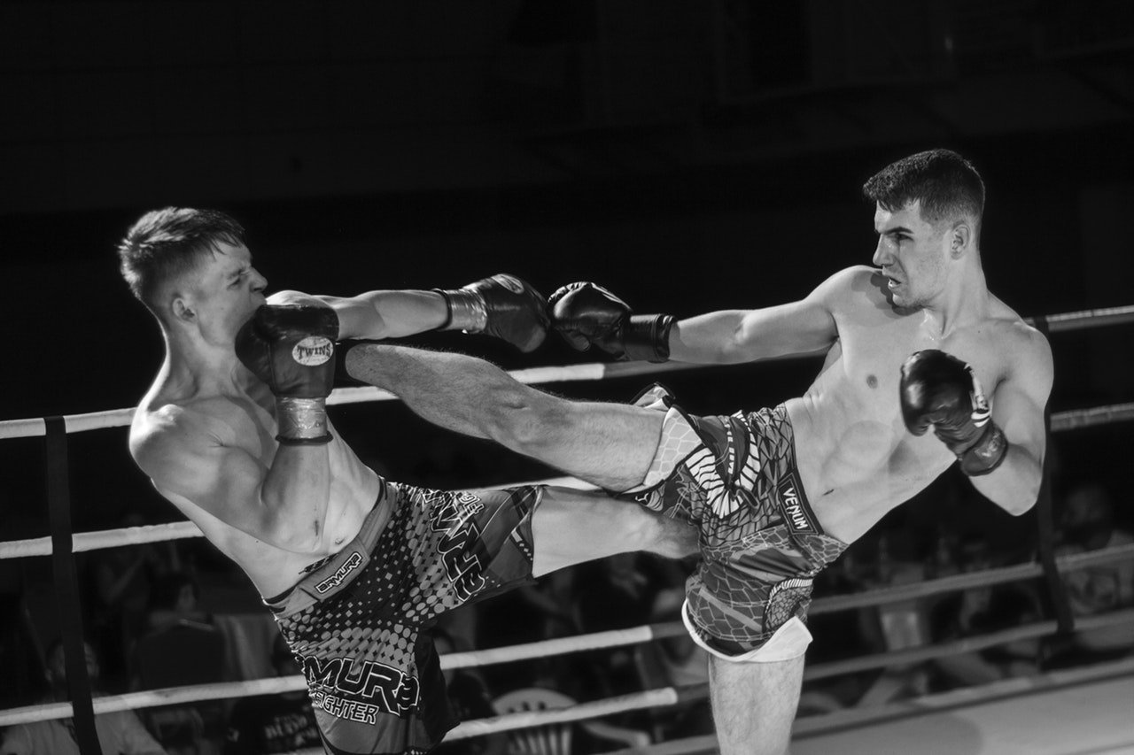 Dois homens lutando dentro de um ringue. Ambos usam luvas de boxe e shorts.