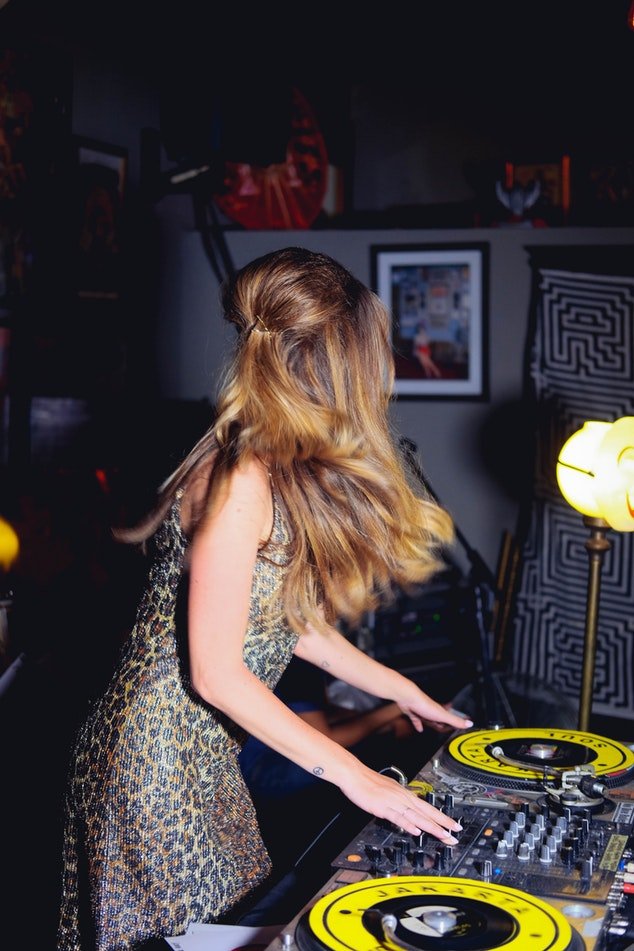Mulher de vestido e cabelos longos girando os discos de som em uma festa.