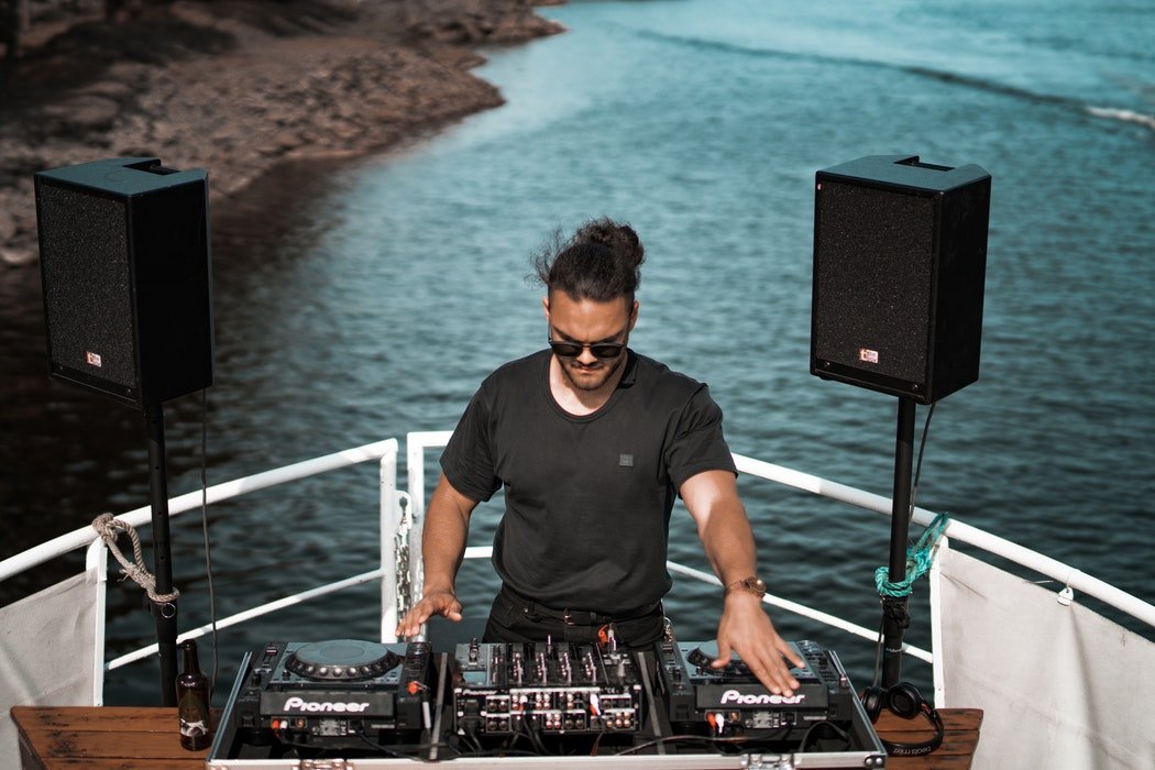 DJ trabalhando na mesa de som de um barco, de frente para o mar.