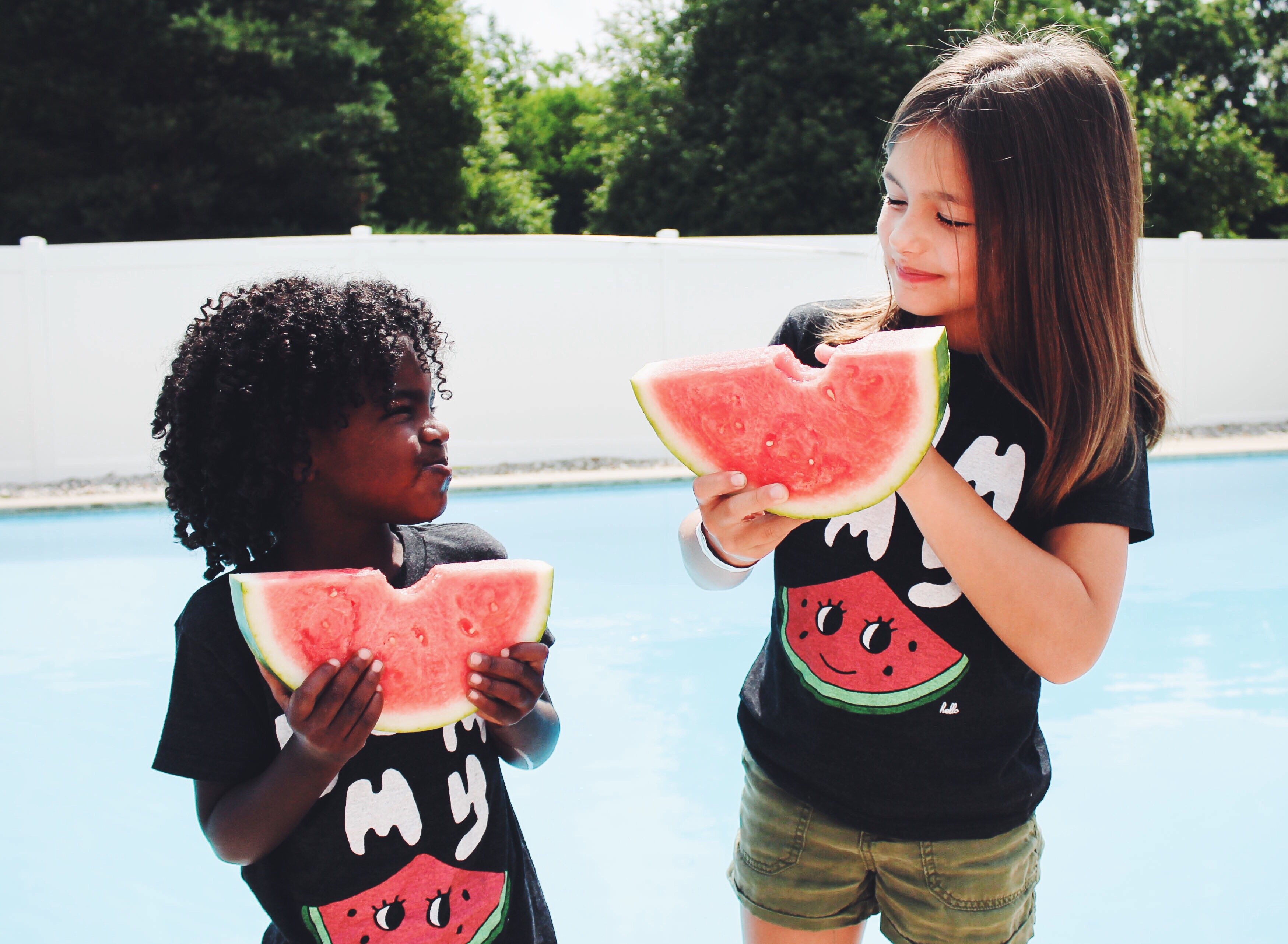Duas crianças comendo melancia ao lado de uma piscina
