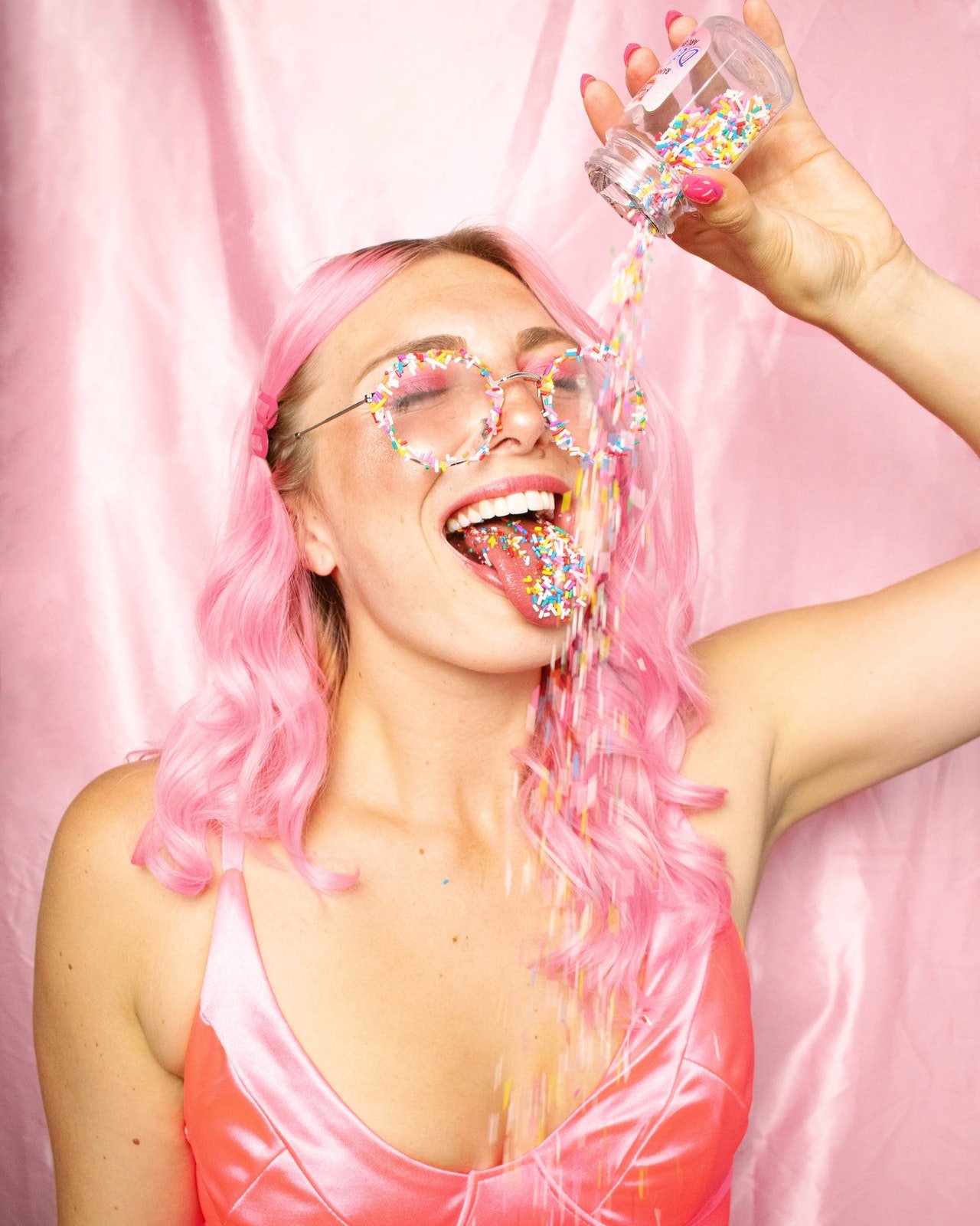 Mulher de roupa e cabelos cor de rosa comendo doces coloridos