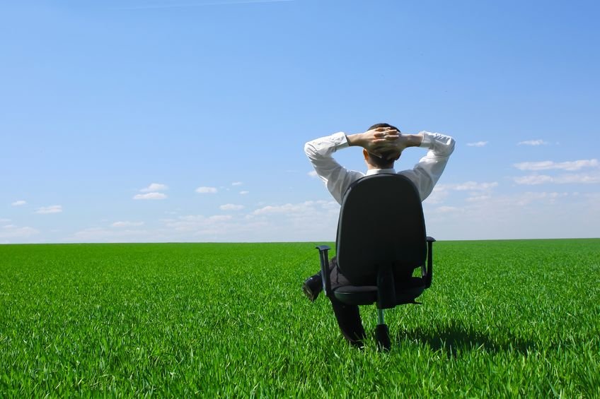 Homem sentado em cadeira de escritório em campo verde com céu azul ao fundo