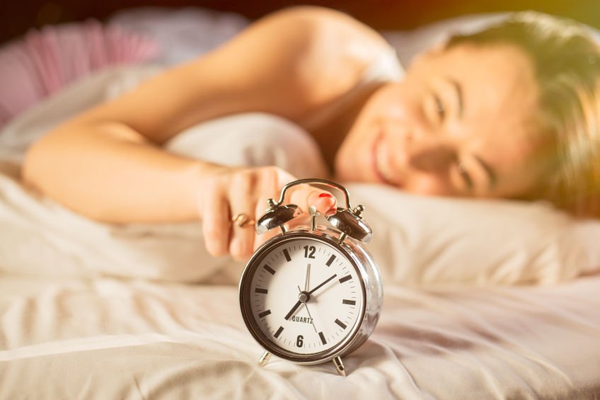 Mulher sorrindo na cama apertando botão de relógio em cama