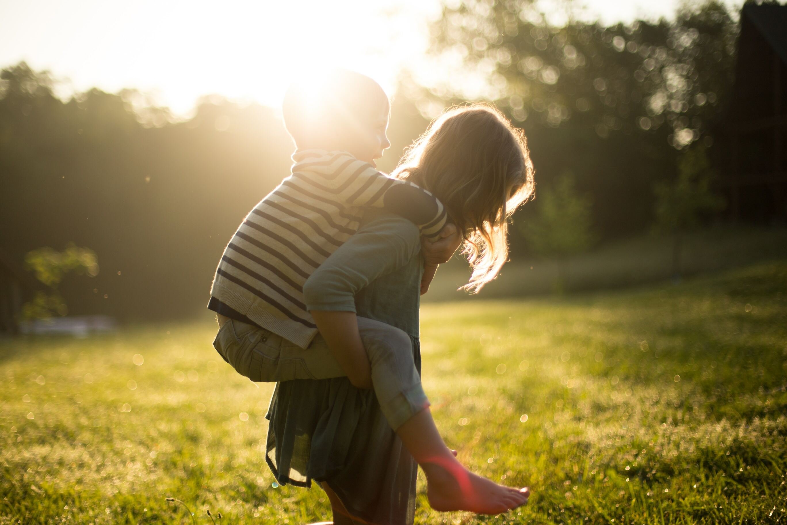 Menina jovem carregando menino pequeno em suas costas durante o dia, em um gramado.