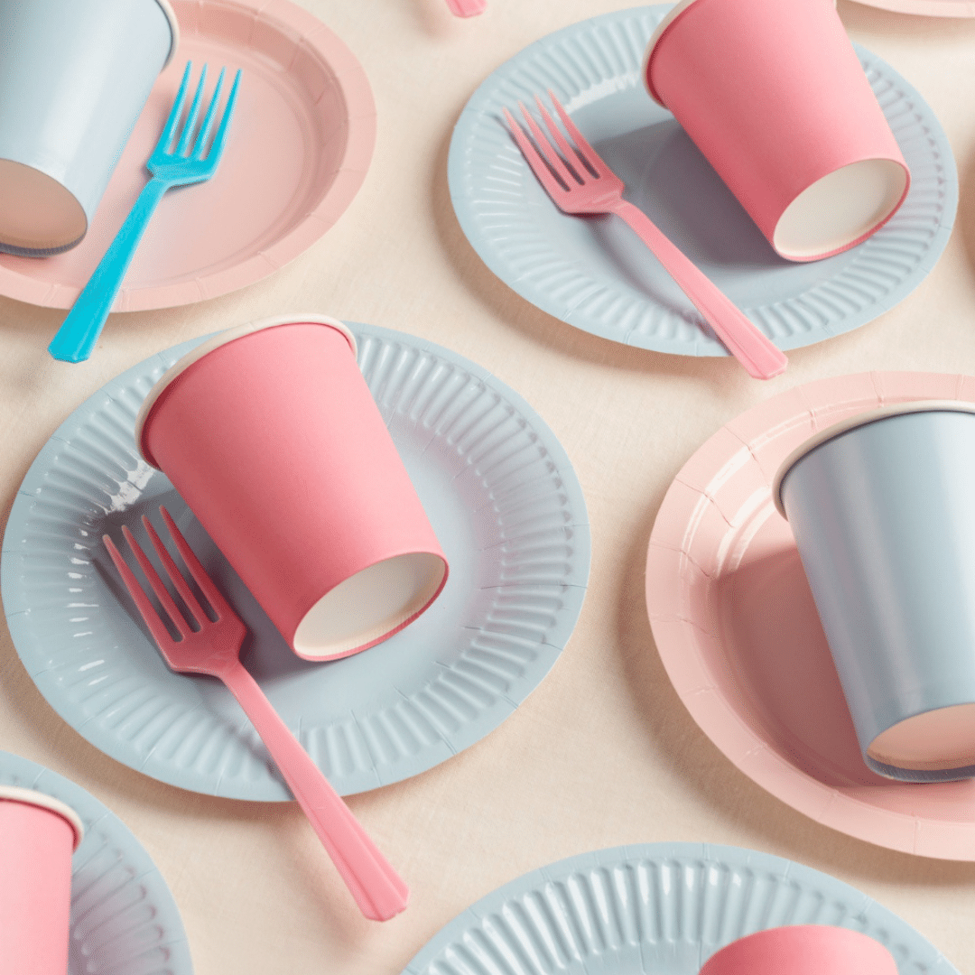 Mesa arrumada com vários copos, pratos e talheres de plástico nas cores rosa e azul